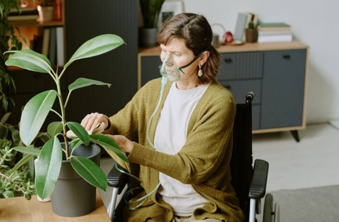 Woman in a wheelchair taking care of a potted plant with an oxygen mask