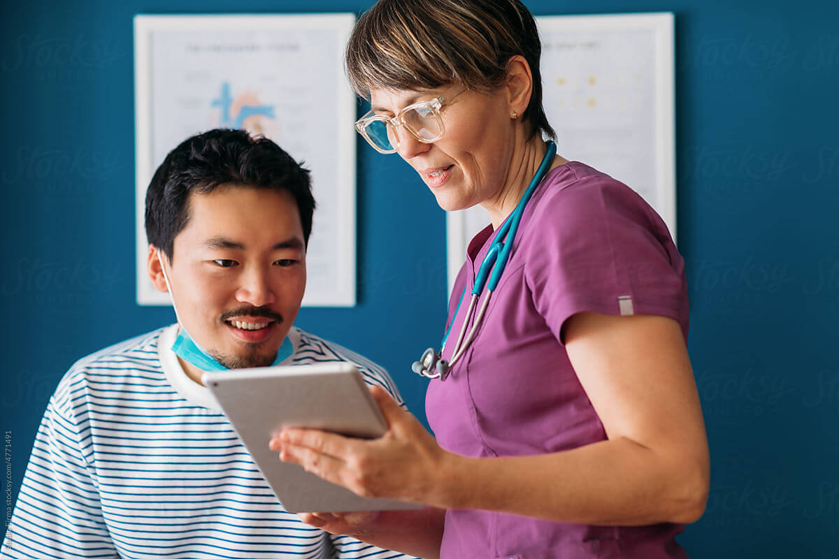 Doctor in scrubs showing a digital tablet to a patient in a medical office