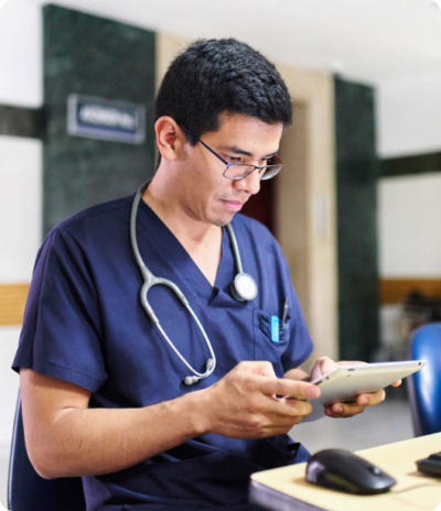 Male nurse using a tablet in a hospital setting wearing blue scrubs and a stethoscope