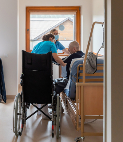 Healthcare workers assist patient in wheelchair near hospital bed in bright room